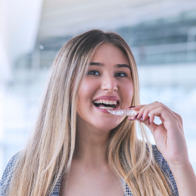Young woman smiling while holding clear aligner, modern office building background