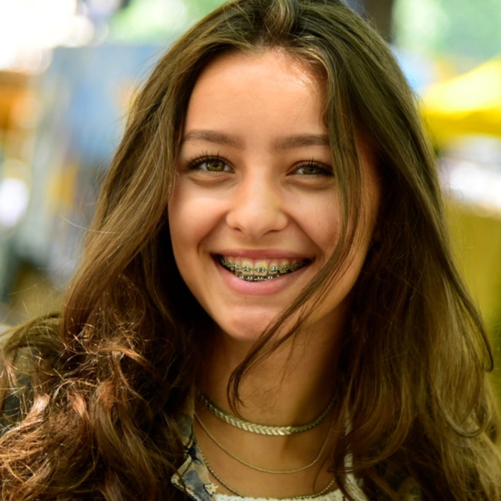 Smiling young woman wearing pearl necklace in orthodontic office setting, displaying healthy teeth.
