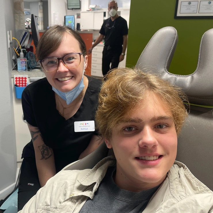 Two staff members smiling at camera in modern orthodontic office with green walls.